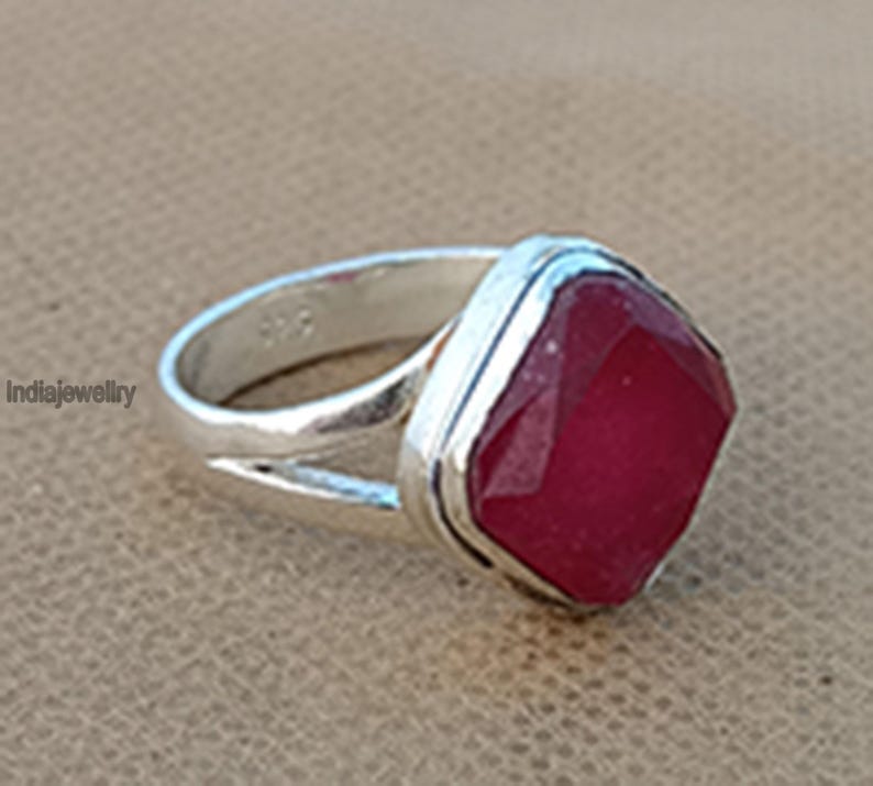Op de afbeelding: Een zilveren ring met een grote, vierkante, gefacetteerde, rode edelsteen. De ring heeft een eenvoudige band met een gesplitst ontwerp.
