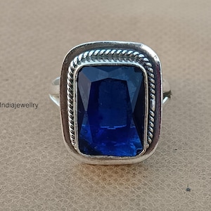 Könnte beinhalten: Ein silberner Ring mit einem großen, dunkelblauen Edelstein, der in einer quadratischen Fassung sitzt. Die Fassung hat einen seilartigen Rand.