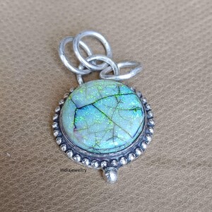 May include: A round, silver pendant with a large, iridescent opal stone. The opal has a cracked, leaf-like pattern with shades of blue and green. The pendant has a beaded silver border and a silver bail.