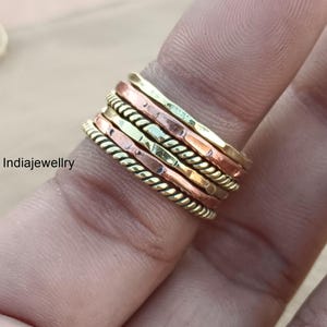 May include: A set of seven stacking rings made of copper, brass, and gold-toned metal. The rings have different textures, including hammered, twisted, and smooth.