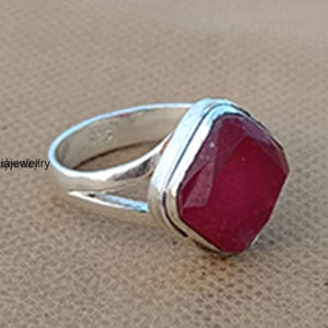 Op de afbeelding: Een zilveren ring met een grote, gefacetteerde, rode edelsteen gezet in een vierkante zetting. De ring heeft een eenvoudige band met een gesplitst ontwerp.