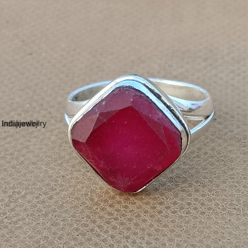 Op de afbeelding: Een zilveren ring met een grote, vierkante, rode edelsteen in het midden. De ring heeft een eenvoudig, elegant ontwerp.