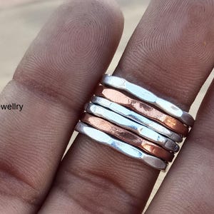 May include: A stack of five silver and copper rings, worn on a finger. The rings are hammered and have a textured finish.