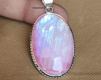 Op de afbeelding: Ovale hanger met een grote, iriserende roze en blauwe edelsteen. De steen is gezet in een zilverkleurig metalen frame met een getextureerde rand en een zilveren balein. De hanger wordt door een vinger vastgehouden.