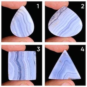 Puede incluir: Cuatro piedras preciosas pulidas de ágata de encaje azul en diferentes formas: gota, corazón, cuadrado y triángulo. Cada piedra muestra un patrón de bandas azul claro y oscuro, sostenidas entre los dedos sobre un fondo negro.