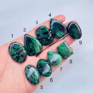 May include: Nine polished ruby in zoisite gemstones of various shapes and sizes, labelled with numbers one through nine. Each stone features a vibrant green base with dark black inclusions and distinct patches of deep magenta or reddish-pink colour.