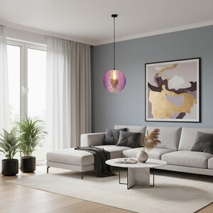 Peut inclure: Une suspension sphérique dotée d'un abat-jour en verre violet translucide et texturé, suspendue par un fin cordon noir. La lampe émet une lueur chaude depuis l'intérieur, mettant en valeur la surface inégale et alvéolée du globe en verre.