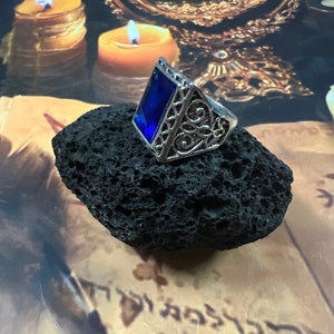 May include: A silver ring with a blue rectangular gemstone set in a decorative filigree design.