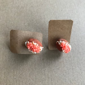 May include: A pair of handmade polymer clay earrings featuring a brown base with a pink and white design. The earrings are displayed on brown card stock.
