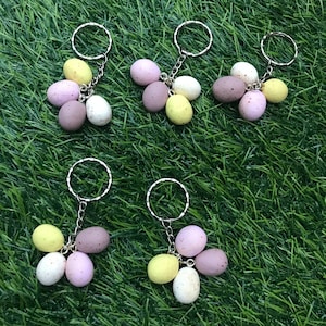 May include: Six keychains with three pastel-coloured eggs attached to each. The eggs are in shades of pink, yellow, and brown. The keychains are silver.