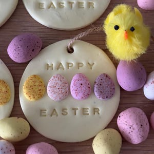 May include: A yellow chick ornament with a white background that says "Happy Easter" and has a row of speckled Easter eggs on the bottom.
