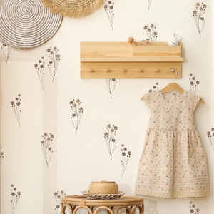 Può includere: Un muro bianco con uno scaffale in legno e ganci, una piccola statuetta di coniglio bianco e un vestito beige con motivo floreale. Il muro è decorato con piccoli adesivi floreali marroni.