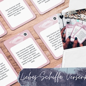 May include: Pink cards with the text "Vorspiel" and instructions for a couples game. The cards are on a wooden surface. The text on the cards is in German.