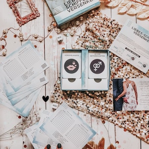 May include: A blue and white game box with the title "Liebes-Schiffe Versenken" and a picture of a couple on the front. The game includes a set of cards with the words "Vorspielkarte" and "Intime Aktionskarten".