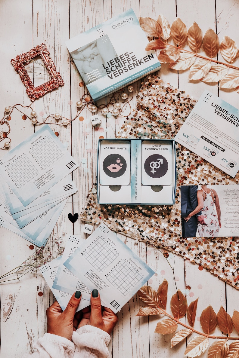 May include: A blue and white game box with the title "Liebes-Schiffe Versenken" and a picture of a couple on the front. The game includes a set of cards with the words "Vorspielkarte" and "Intime Aktionskarten".