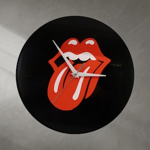Könnte beinhalten: Eine schwarze Wanduhr mit dem roten und weißen Zungen- und Lippenlogo der Rolling Stones. Die Zeiger sind weiß, und das Zifferblatt ist eine wiederverwendete Schallplatte. Ein einzigartiges Stück Rock'n'Roll-Dekoration.