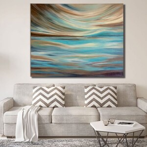 Puede incluir: Pintura abstracta con una combinación de colores azules y marrones. La pintura representa un paisaje con una línea de horizonte y un cielo con nubes. La pintura se muestra en una pared sobre un sofá gris.