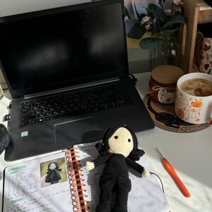 May include: A white ceramic mug with a black handle and the text "But First, Coffee" in a bold, black font. The mug is set against a blurred background. The mug is approximately 10 cm tall.