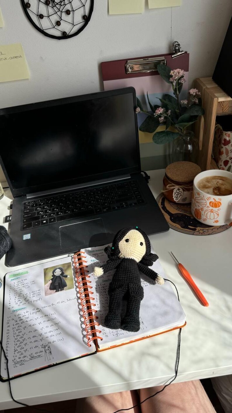 May include: A white ceramic mug with a black handle and the text "But First, Coffee" in a bold, black font. The mug is set against a blurred background. The mug is approximately 10 cm tall.