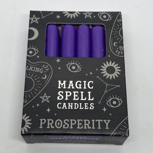 May include: A box of purple magic spell candles for prosperity. The box has a black background with silver stars, moons, and eyes. The text on the box reads "Magic Spell Candles" and "Prosperity".