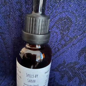 May include: A small brown glass bottle with a black dropper. The label reads "Spells by Sarah, Bespoke Bach Essence Blend." The bottle contains a liquid and is set against a textured blue background. The bottle is 30ml.