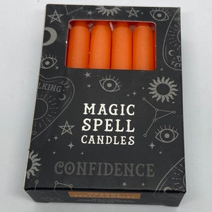 May include: A box of orange magic spell candles for confidence. The box has a black background with white stars, a sun, and an eye design. The text on the box reads "Magic Spell Candles" and "Confidence".