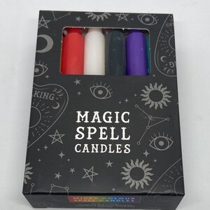 May include: A box of Magic Spell Candles with a black background and silver stars, moons, and eyes. The box contains six candles in red, white, black, purple, and teal.