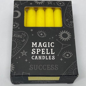 May include: A box of yellow magic spell candles for success. The box has a black background with white stars, a crescent moon, and a sun. The text on the box reads "Magic Spell Candles" and "Success".