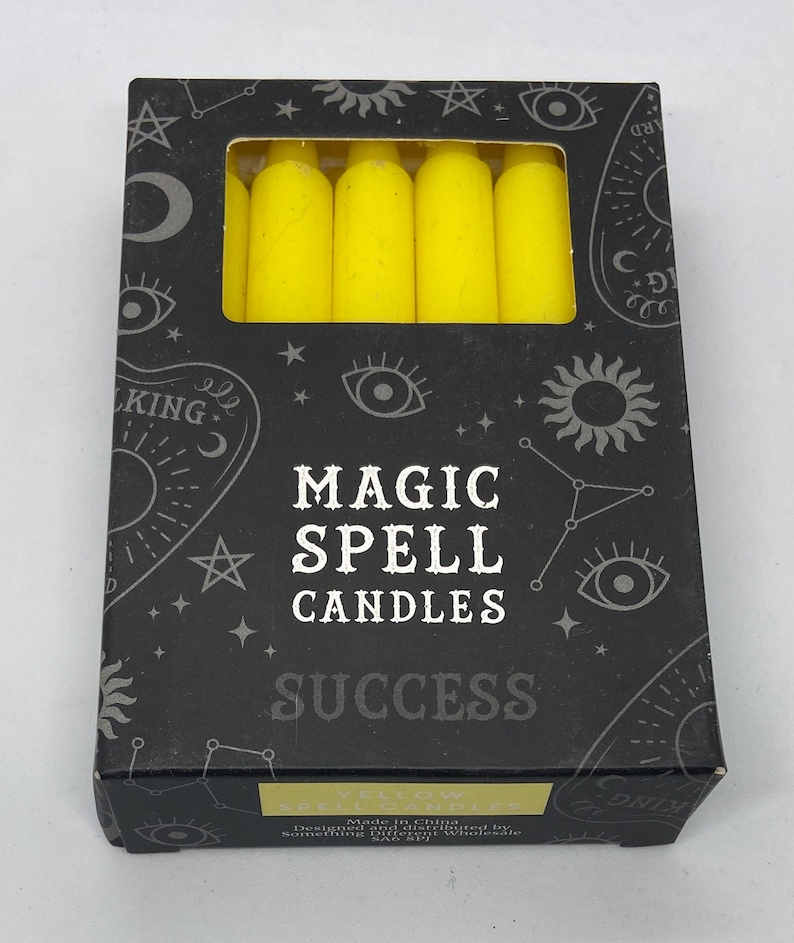 May include: A box of yellow magic spell candles for success. The box has a black background with white stars, a crescent moon, and a sun. The text on the box reads "Magic Spell Candles" and "Success".
