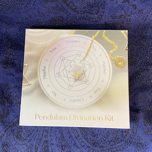 Könnte beinhalten: Ein weiß-goldenes Pendel-Divinationsset mit einem Kristallpendel an einer Kette. Das Set enthält ein kreisförmiges Diagramm mit den Worten "Ja", "Nein", "Vielleicht" und "Unsicher" darauf.