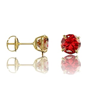May include: A pair of gold stud earrings with a red gemstone in the center. The earrings have a screw-back closure.