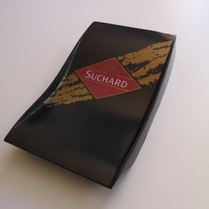 May include: A black box with a gold and red label that says "Le Chocolatier Suchard".