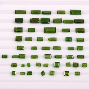 May include: A collection of green gemstones, cut into rectangular shapes, arranged on a white surface. The gemstones are of varying sizes and are likely to be used for jewellery making.