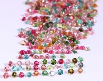 Puede incluir: Una colección de piedras preciosas de colores, incluyendo rosa, verde, azul y naranja, dispuestas en un montón suelto sobre una superficie blanca.
