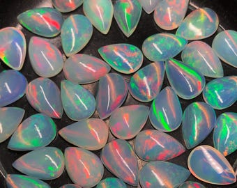 May include: A collection of pear-shaped opals with iridescent colors of red, green, and blue. The gemstones are displayed against a dark background, showcasing their polished surfaces and internal play-of-color. These opals are ideal for jewelry making.