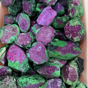 Peut inclure: Un ensemble de pierres brutes de rubis-zoïsite. Les pierres présentent un mélange de couleurs vives, avec des inclusions de rubis magenta profond sur un fond de zoïsite verte. Les pierres varient en taille et en forme.