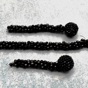 May include: Three black beaded necklaces with large round black beads at the ends.