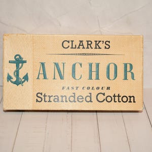 Könnte beinhalten: Rechteckiges Schild mit dem Text "CLARK'S ANCHOR FAST COLOUR Stranded Cotton". Das Schild hat eine türkisfarbene Ankergrafik. Der Hintergrund ist beige.