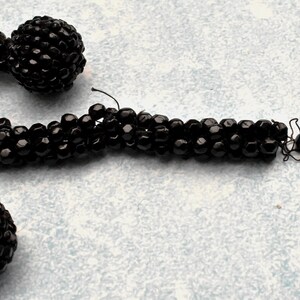 May include: A black beaded necklace with two large black bead accents. The necklace is made of small, round beads that are strung together to create a long, flowing strand.