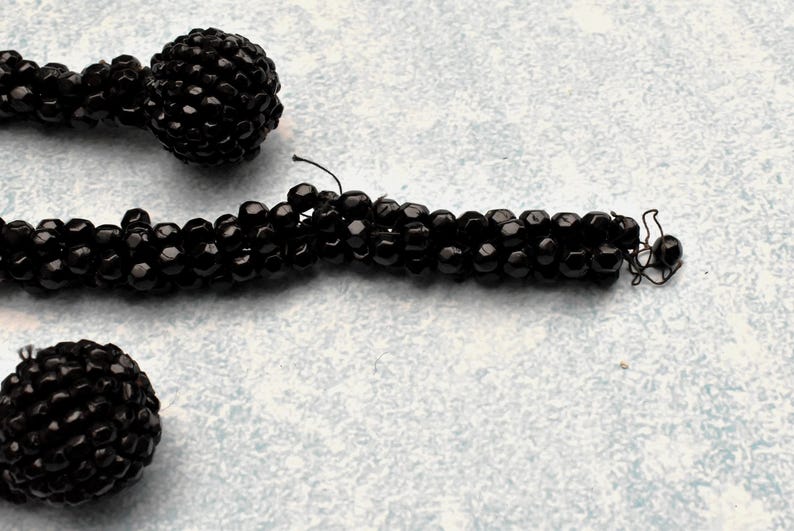 May include: A black beaded necklace with two large black bead accents. The necklace is made of small, round beads that are strung together to create a long, flowing strand.