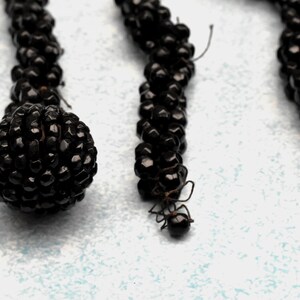 May include: A close-up of three black beaded necklaces. The beads are small and round, and they are strung together in a tight, even pattern. The necklaces are hanging against a white background.