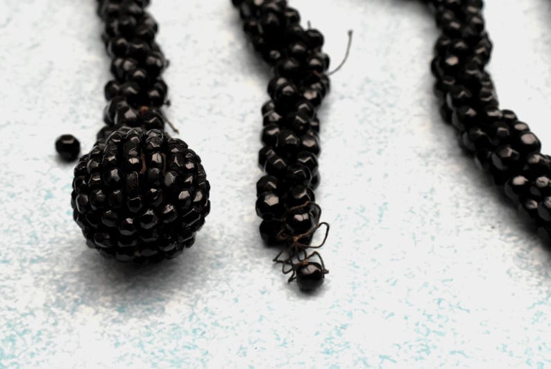 May include: A close-up of three black beaded necklaces. The beads are small and round, and they are strung together in a tight, even pattern. The necklaces are hanging against a white background.
