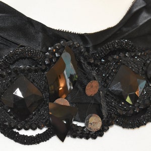 Puede incluir: Tela de sat&eacute;n negro con un adorno decorativo de cuentas y diamantes de imitaci&oacute;n negros. El adorno presenta piedras negras grandes y facetadas.