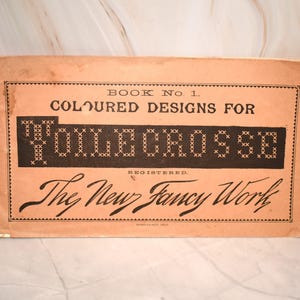 May include: Vintage book cover, "Book No. 1 Coloured Designs for Yolle Cross St." in black text on a peach background. The title "The New Fancy Work" is in cursive. The cover has a decorative border.