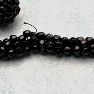 May include: A close-up of a black beaded necklace. The beads are small and round, and they are strung together on a thin thread. The necklace is lying on a white surface.
