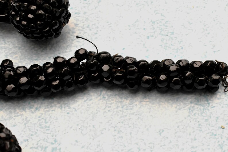 May include: A close-up of a black beaded necklace. The beads are small and round, and they are strung together on a thin thread. The necklace is lying on a white surface.