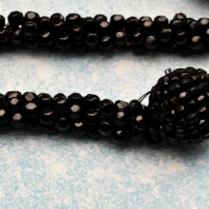 May include: A black beaded necklace with a large black beaded pendant. The beads are small and round, and the pendant is made of many smaller beads.