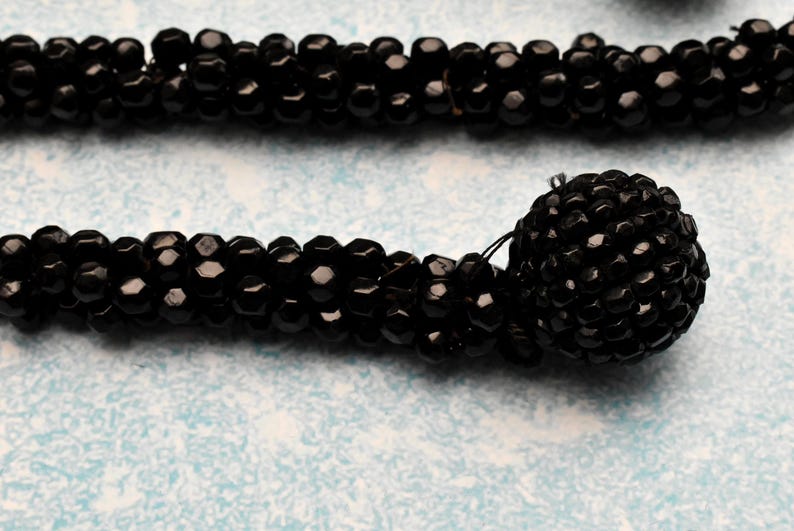May include: A black beaded necklace with a large black beaded pendant. The beads are small and round, and the pendant is made of many smaller beads.