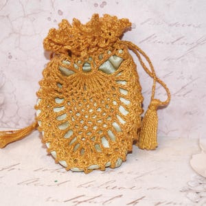May include: A small, handmade drawstring pouch with a golden-yellow crocheted exterior. The pouch features a delicate, openwork design and a matching tassel. The interior appears to be a light green fabric. The pouch is likely used for small items.