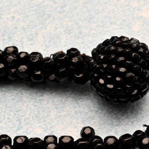 May include: A black beaded necklace with a large black bead at the end. The beads are small and round, and the necklace is made of a single strand.